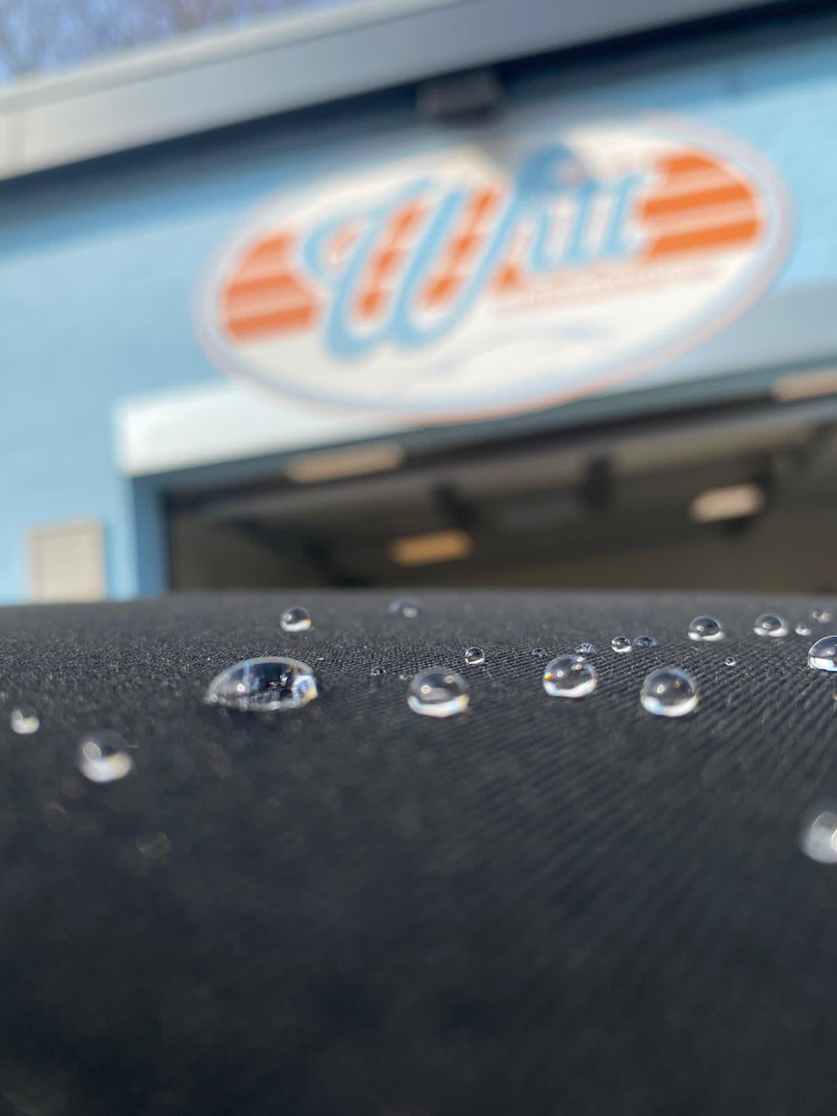 Abperlendes Wasser auf versiegeltem Lack, im Hintergrund das Witt-Logo in der Werkstatt